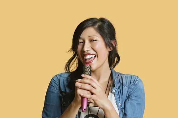 Portrait of a young woman singing into a hairbrush over colored background — Stock Photo, Image