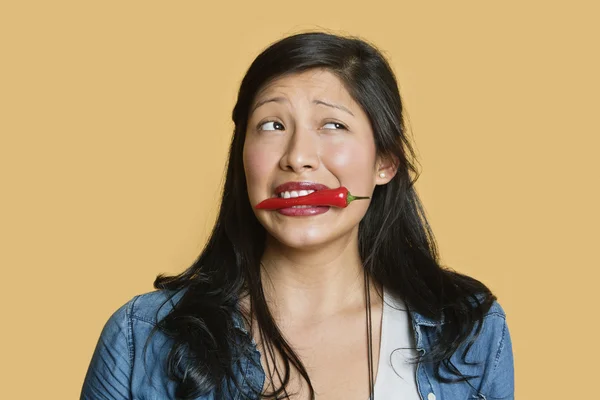 Jonge vrouw met rode chili peper in mond over gekleurde achtergrond — Stockfoto