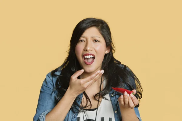 Retrato de una mujer joven comiendo chile rojo picante sobre fondo de color — Foto de Stock