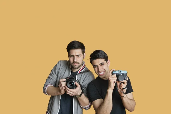 Portrét mladých mužských přátel s digitálním fotoaparátem nad barevným pozadím — Stock fotografie
