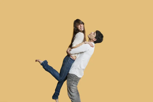 Happy young man carrying girlfriend over colored background — Stock Photo, Image