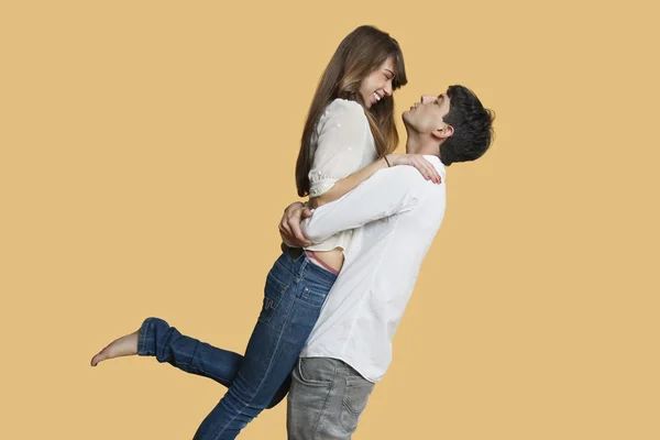 Side view of young couple looking at each other while man carrying girlfriend over colored background — Stock Photo, Image