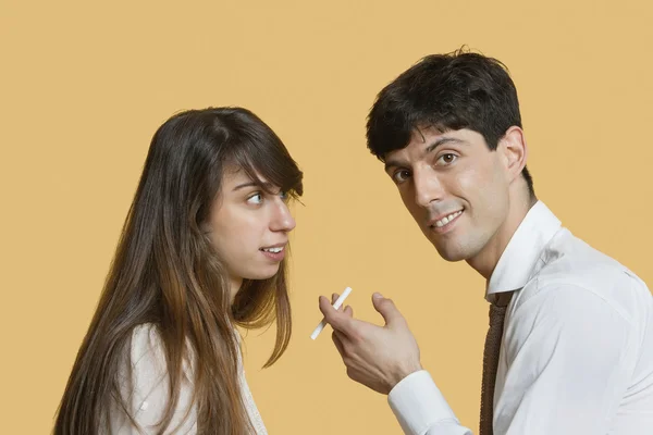 Portrait of a young man with cigarette while woman looking at him over colored background — Stock Photo, Image