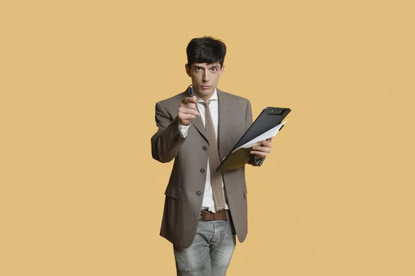 Portrait of a young businessman pointing while holding clipboard over colored background — Stock Photo, Image