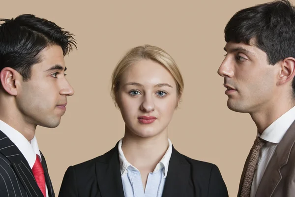 Porträt einer jungen Geschäftsfrau mit männlichen Kollegen, die sich vor farbigem Hintergrund anstarren — Stockfoto