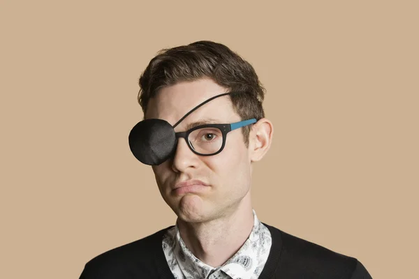 Portrait of a man wearing eye patch on glasses over colored background — Stock Photo, Image