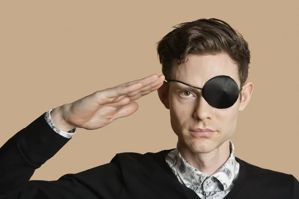 Portrait of a man wearing eye patch saluting over colored background — Stock Photo, Image