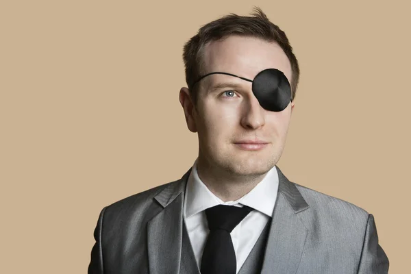Close-up of a young businessman with eye patch looking away over colored background — Stock Photo, Image