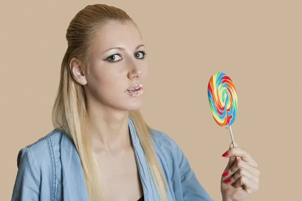 Porträtt av en blond kvinna med beströdda läppar hålla lollipop över färgad bakgrund — Stockfoto