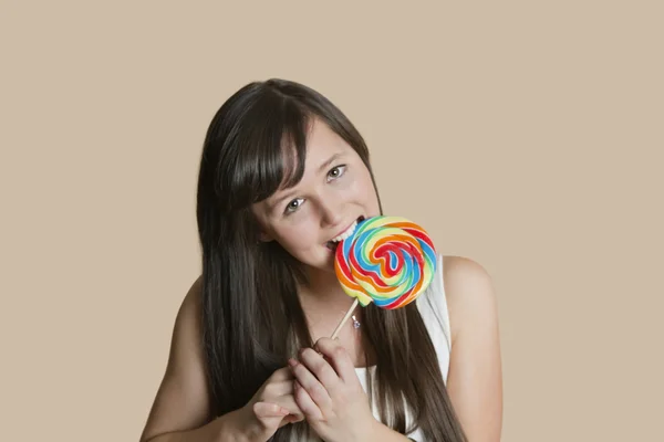 Portrait of beautiful young woman biting lollipop over colored background — Stock Photo, Image