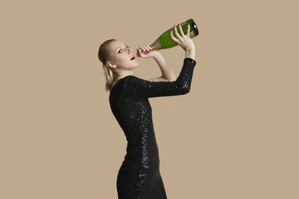 Retrato de una hermosa joven bebiendo champán de botella sobre fondo de color — Foto de Stock