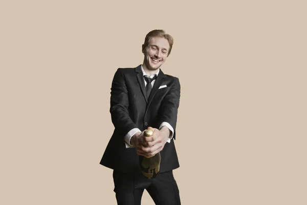 Portrait of a young businessman uncorking champagne over colored background — Stock Photo, Image