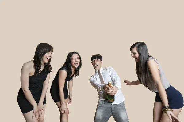 Молодые друзья открывают бутылку шампанского на цветном фоне — стоковое фото