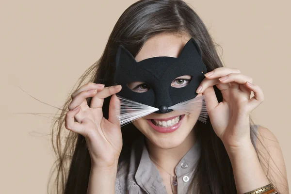 Portrait of a young woman imitating as cat while looking through eye mask over colored background — Stock Photo, Image