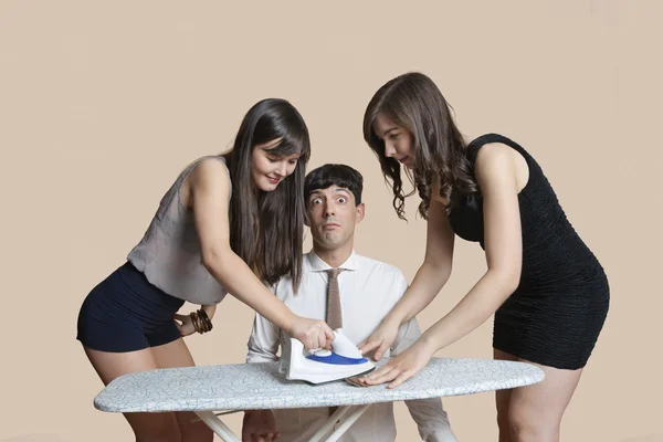 Young women ironing shocked man's tie over colored background — Stock Photo, Image