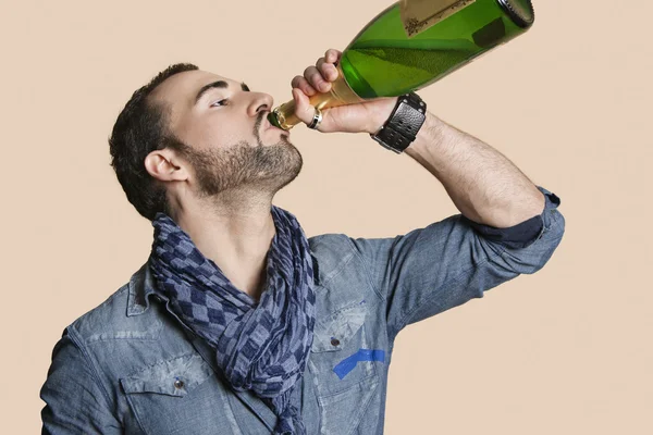 Genç adam şampanya şişesinden renkli arka plan üzerinde içki. — Stok fotoğraf