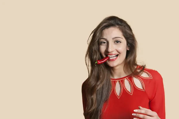 Retrato de una hermosa mujer joven con chile rojo en la boca sobre fondo de color — Foto de Stock
