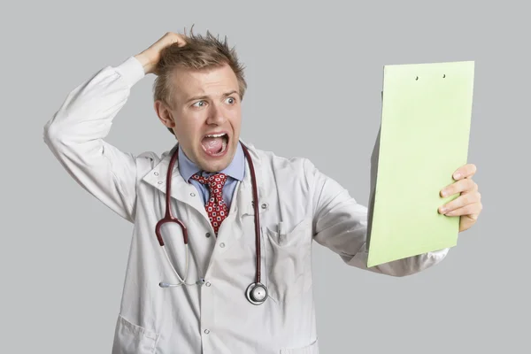 Male doctor terrified looking at medical reports over gray background — Stock Photo, Image