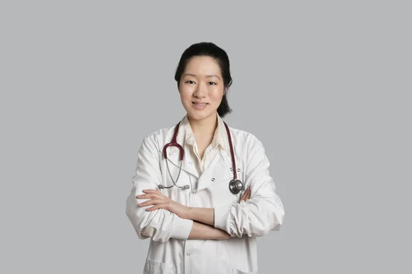 Retrato de una médica asiática de pie con los brazos cruzados sobre fondo gris — Foto de Stock