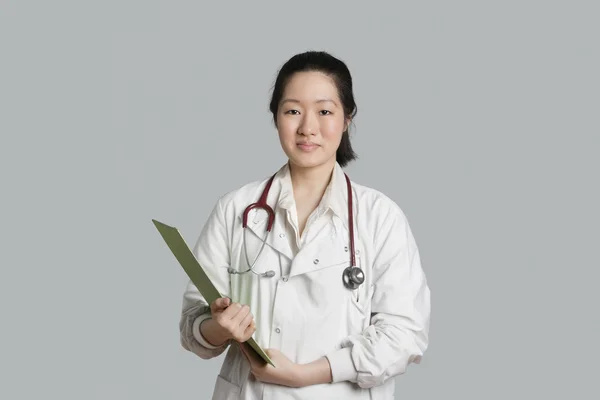 Portrait of an Asian female doctor holding a clipboard over gray background — Stock Photo, Image