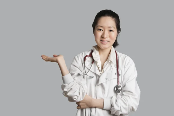 Retrato de uma médica asiática exibindo um produto invisível sobre fundo cinza — Fotografia de Stock