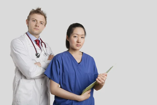 Portret van een Kaukasische arts permanent met een Aziatische verpleegkundige over grijze achtergrond — Stockfoto