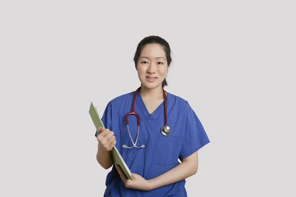 Porträtt av en asiatisk kvinna sjuksköterska hålla Urklipp över grå bakgrund — Stockfoto