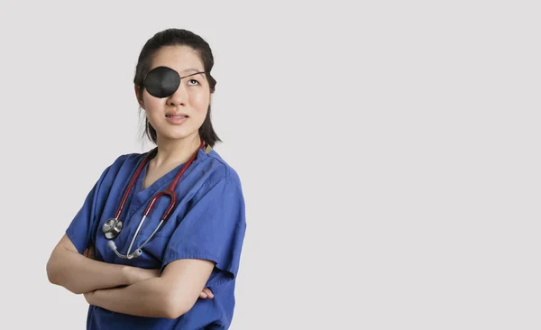 Asiático médico feminino vestindo um remendo olho olhando para cima com os braços cruzados sobre fundo cinza — Fotografia de Stock