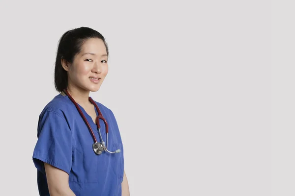 Портрет молодой азиатки-хирурга, улыбающейся на сером фоне — стоковое фото