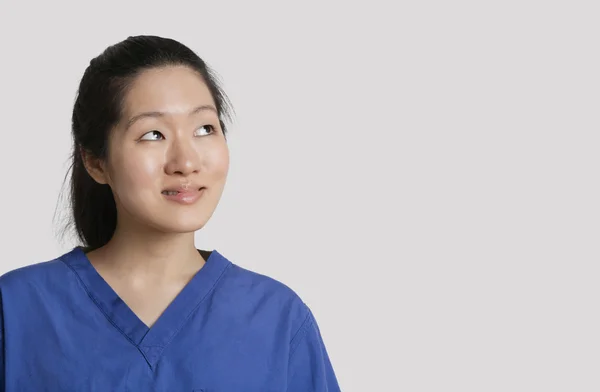 Молодая азиатская женщина-врач смотрит вверх на сером фоне — стоковое фото