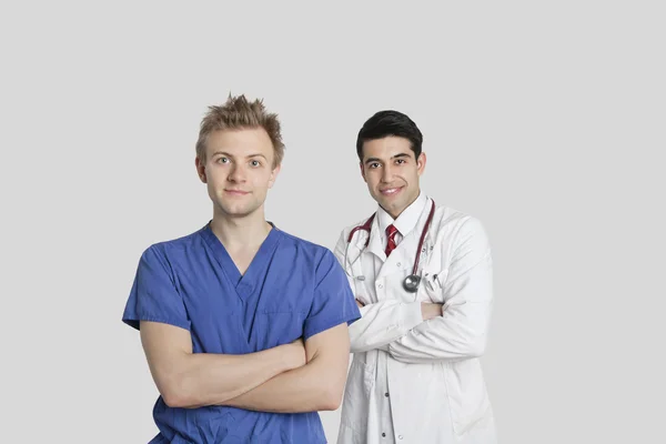 オスの看護婦と医師が腕を組んで灰色の背景の上に立っての肖像画 — ストック写真