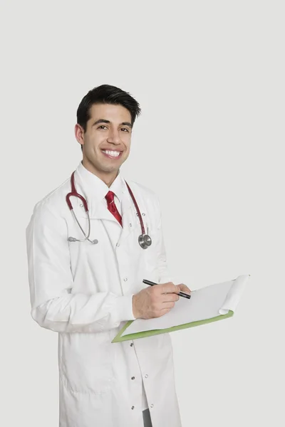 Retrato de un alegre médico indio con una historia clínica sobre fondo gris claro —  Fotos de Stock