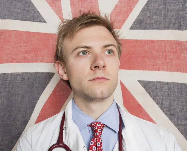Medico caucasico che distoglie lo sguardo dalla bandiera britannica sullo sfondo — Foto Stock