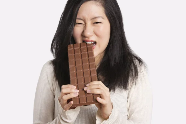 Portrait of a young woman eating a large chocolate bar over light gray background — Stock Photo, Image