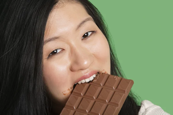 Nahaufnahme Porträt einer jungen Frau, die vor grünem Hintergrund Schokolade isst — Stockfoto