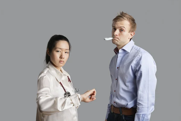 Portrait of a patient with thermometer in mouth standing with doctor — Stock Photo, Image