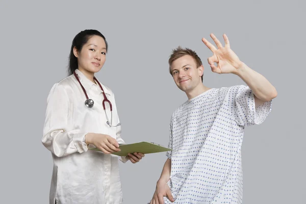 Porträtt av patientens gestikulerande okej med läkare som innehar ett urklipp — Stockfoto