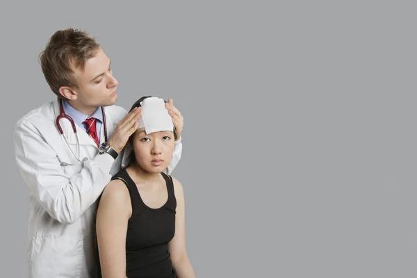 Médico ajustando vendaje en la cabeza del paciente —  Fotos de Stock