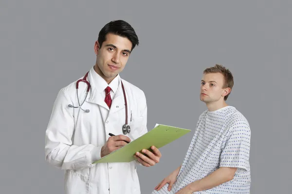 Portrait of Indian doctor writing on clipboard with patient sitting besides — Stock Photo, Image