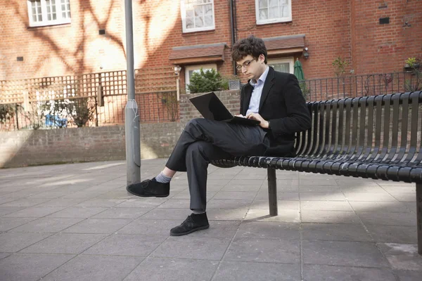 Νέος επιχειρηματίας χρησιμοποιώντας φορητό υπολογιστή ενώ κάθεται σε παγκάκι — Φωτογραφία Αρχείου