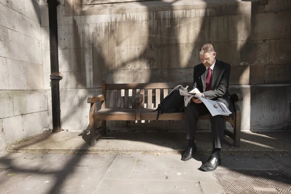 Empresario sentado en el banco al aire libre leyendo el periódico — Foto de Stock