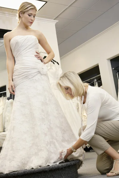 Funcionário sênior ajustando vestido de noiva de bela noiva jovem na loja nupcial Imagens Royalty-Free