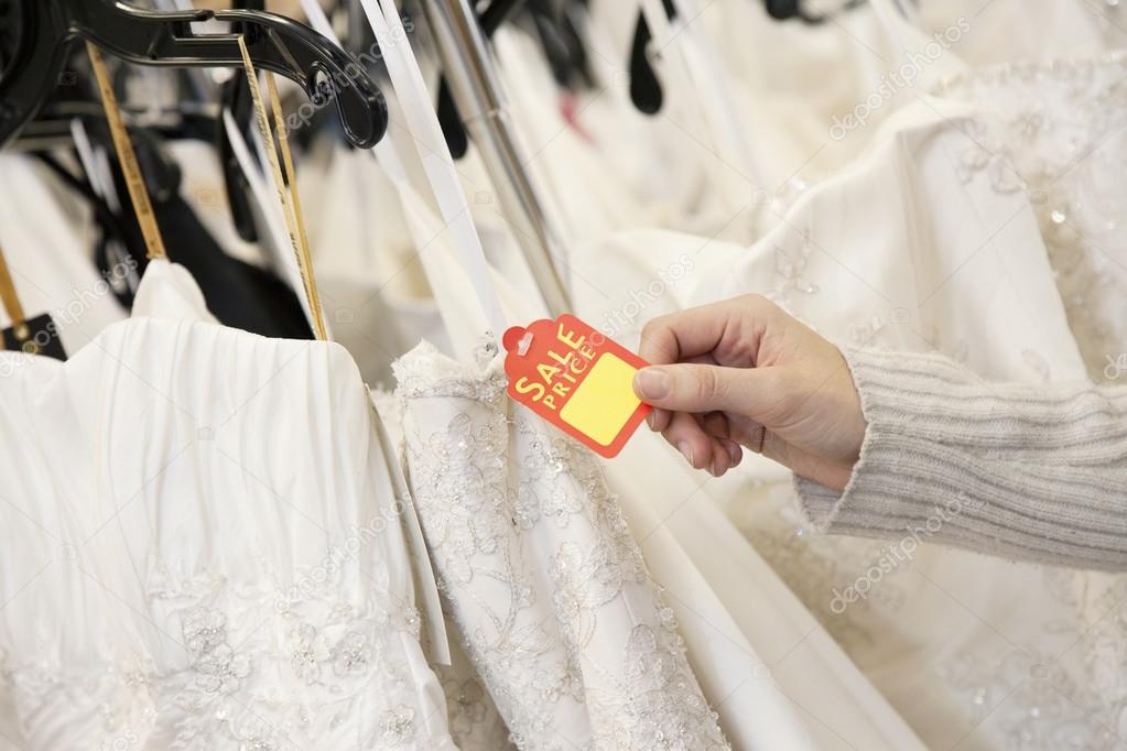 Cropped shot of female hands holding price tag attached to wedding gown in bridal boutique