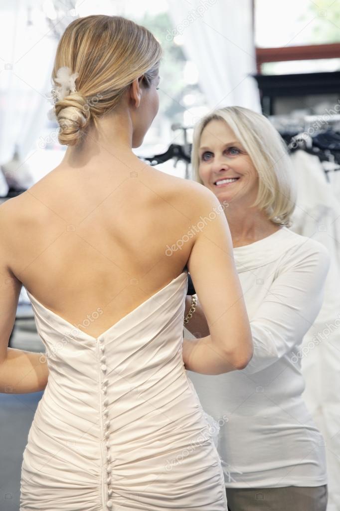 Back view of woman dressed in bridal gown with happy senior owner assisting