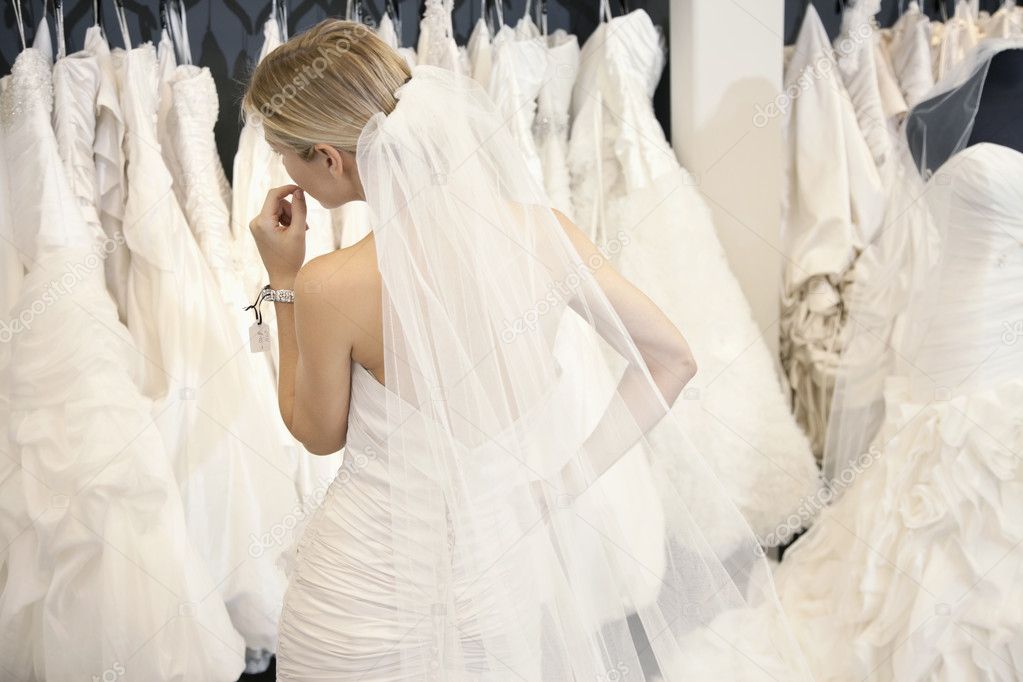 Back view of a young woman in wedding dress looking at bridal gowns on display in boutique