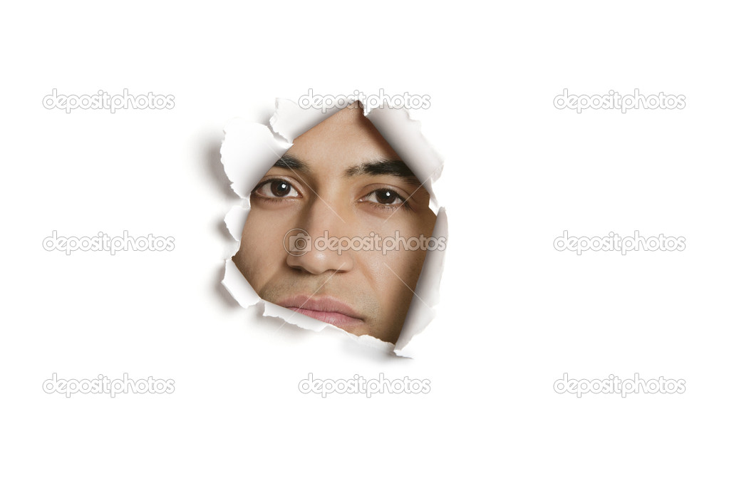 Portrait of a young Indian man peeking from ripped paper hole