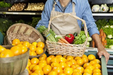 midsection bir süpermarkette sebze sepeti ile portakal durak yakınında duran adam