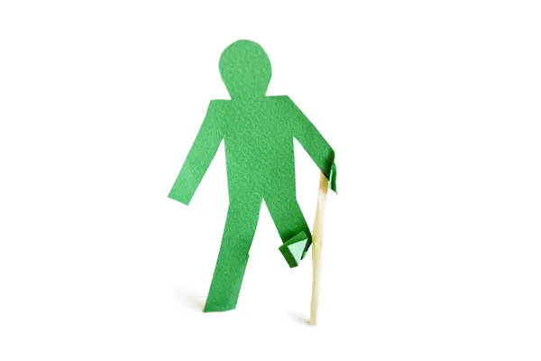 An injured green stick figure with a walking stick over white background — Stock Photo, Image