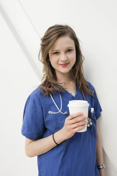 Portrait of a beautiful female doctor holding a disposable cup over colored background — Stock Photo, Image