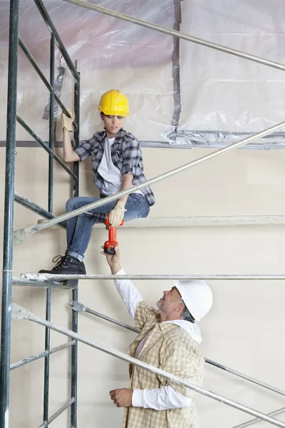 Travailleur masculin donnant foret à la femme sur échafaudage sur le chantier de construction — Photo